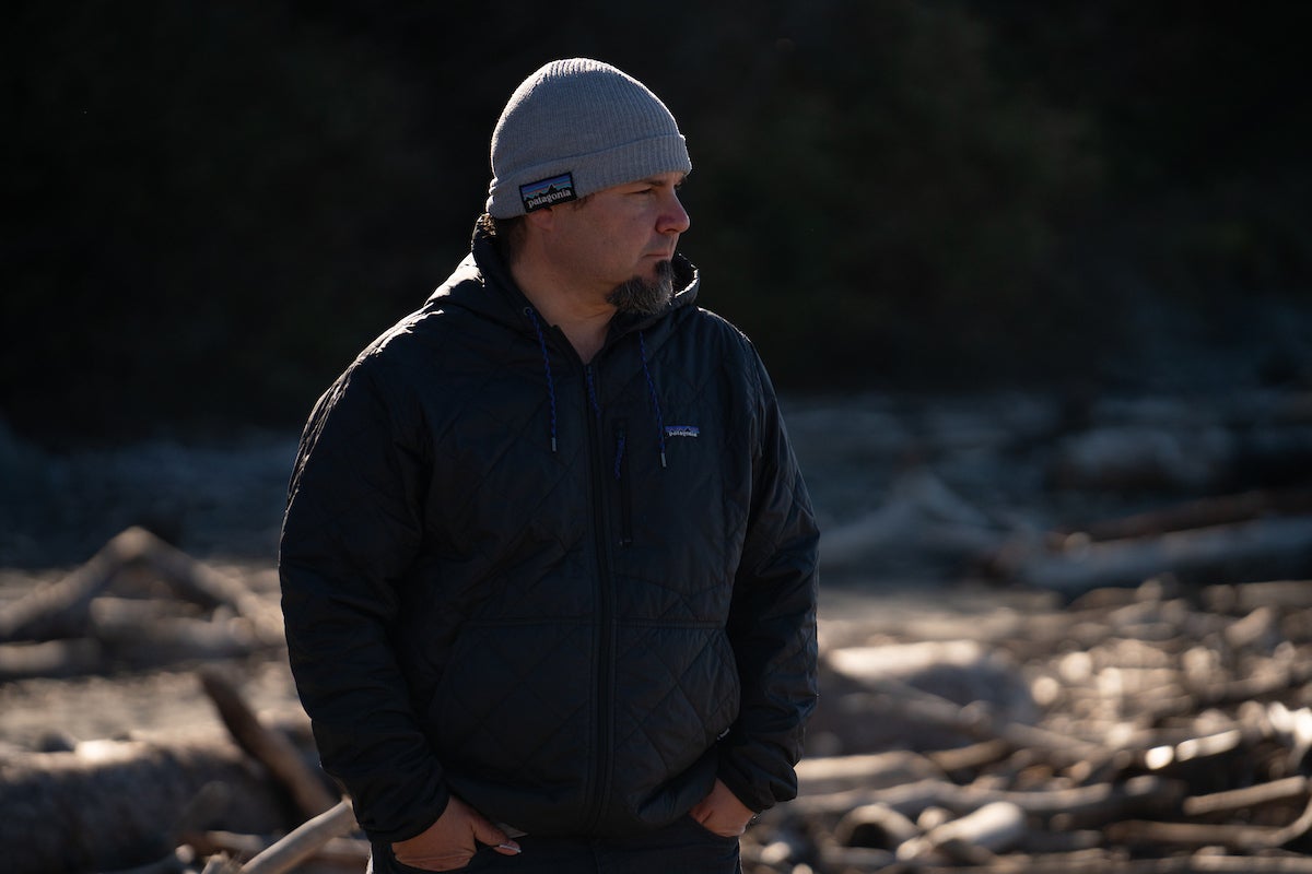 Barry McCovey of Yurok Tribe in gray knit hat, black coat. Driftwood is in background