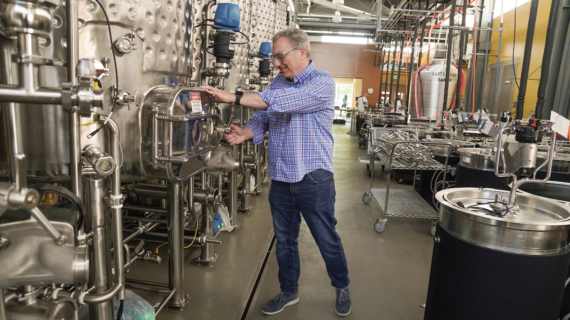 Man stands next to fermentation tanks