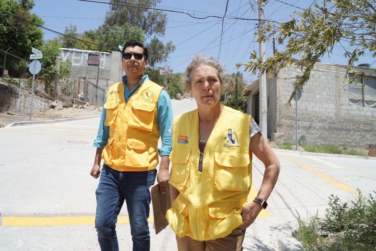 Oscar Zazueta in sunglasses and yellow vest stands with Janet Foley in yellow vest on street in Mexico