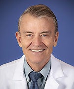 a bio photo of a man, centered in the photo, smiling with short hair and a lab coat