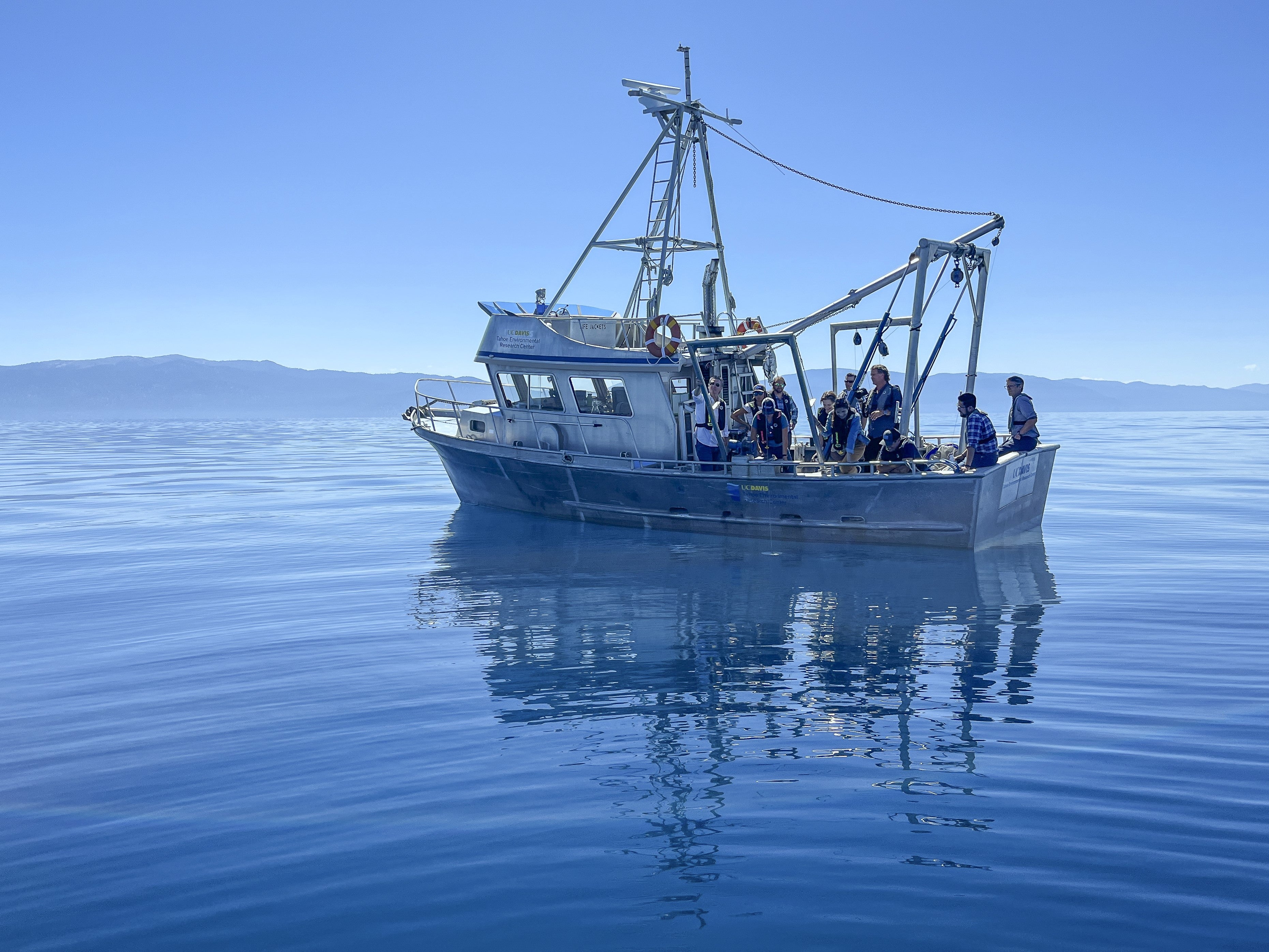 Group of scientists and politicians aboard the UC Davis research vessel under blue skies and on blue water at Lake Tahoe