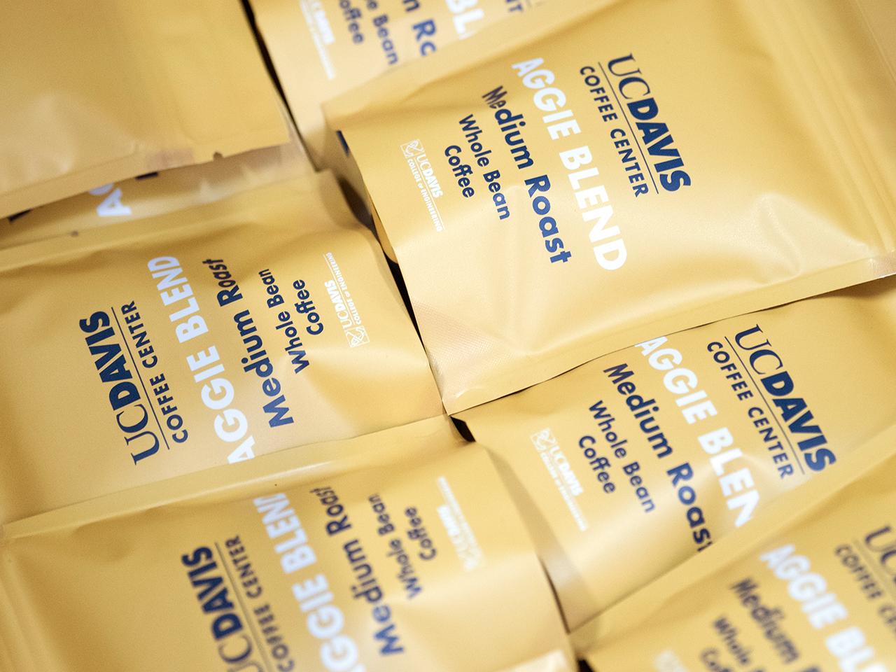 A closeup shot of many bags of coffee in a box. The bags are UC Davis branded in Aggie Gold with Aggie Blue text that says, 