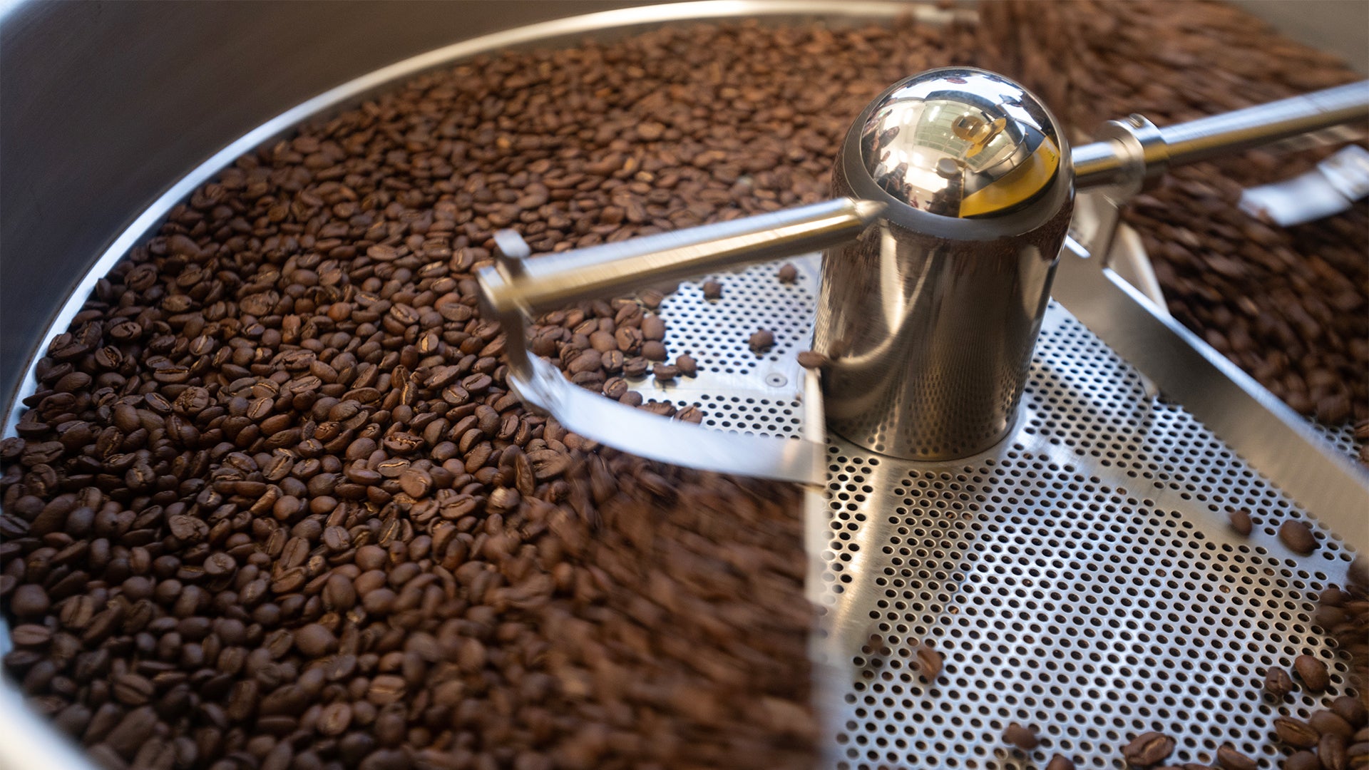 A closeup photo of coffee beans spinning on a roaster's cooling tray.