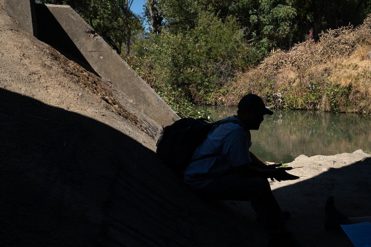 silhouette of man with backpack and hat in concrete tunnel near stream