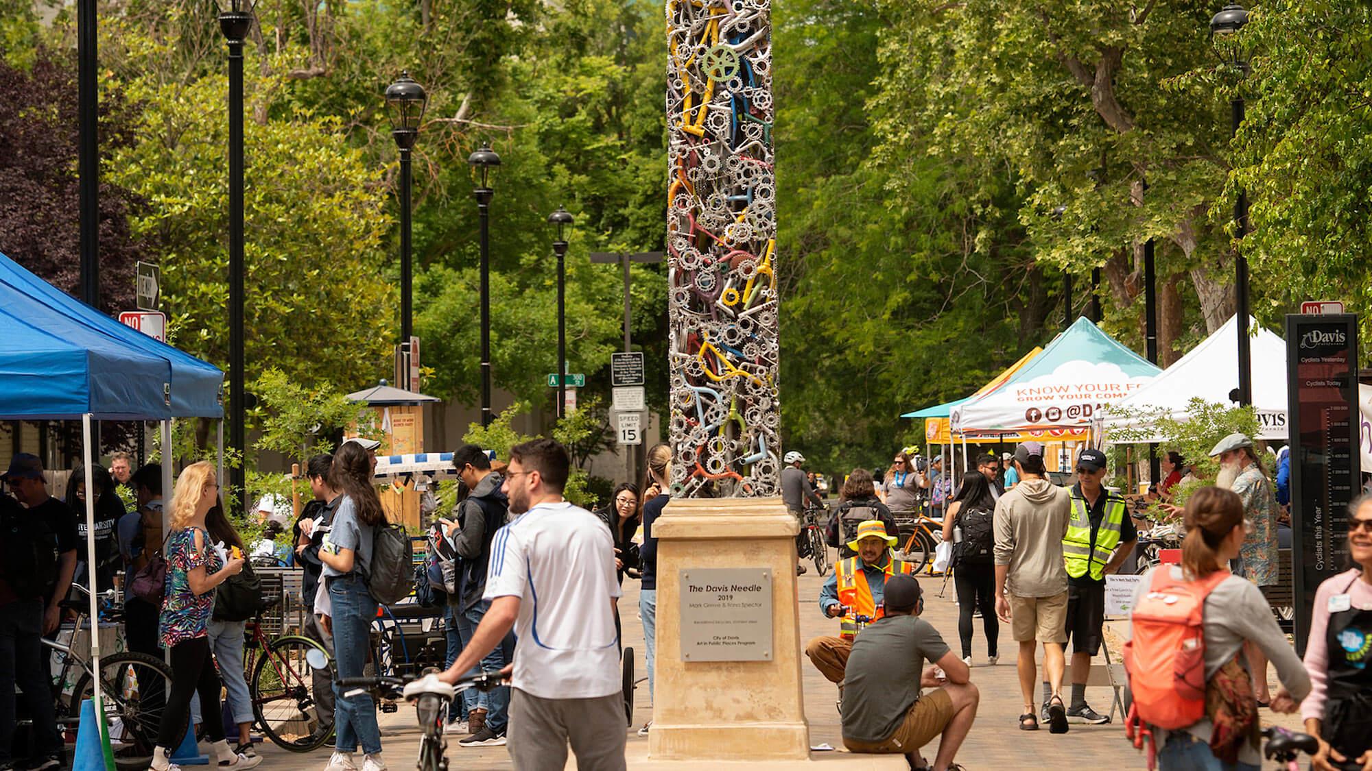 加利福尼亚州戴维斯市中心的一幕，挤满了学生和当地人，还有一座由自行车零件制成的独特方尖碑形雕塑