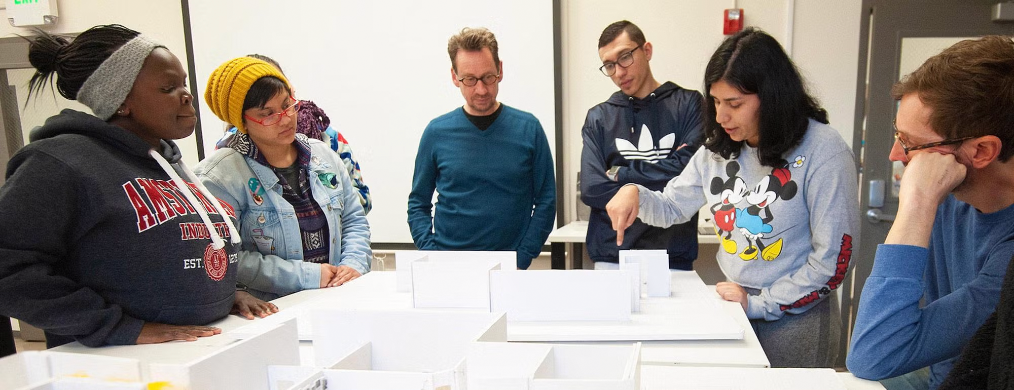 Transfer students standing around a model of a building in a design class