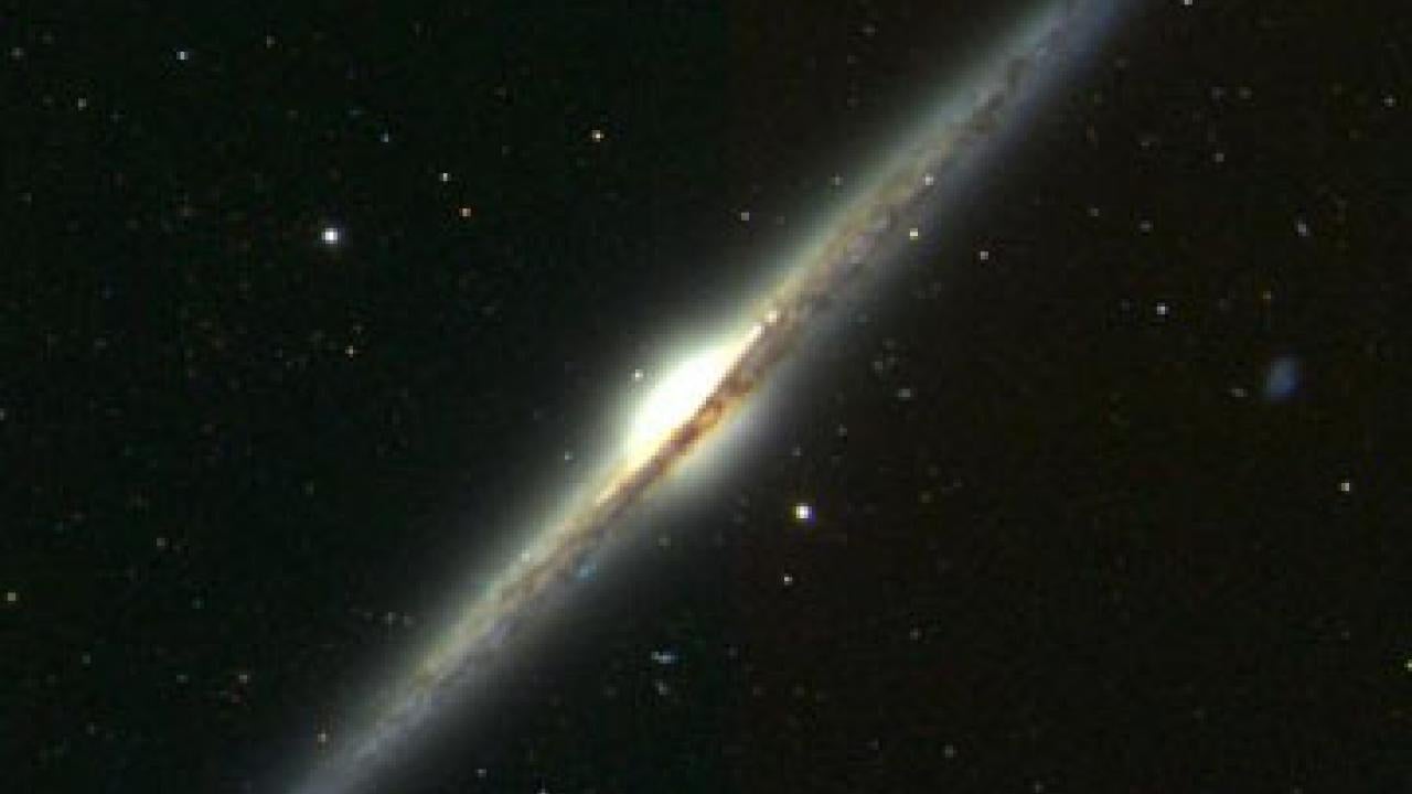 Illustration of galaxy NGC 4565 shows dark lanes of interstellar dust that block sunlight.