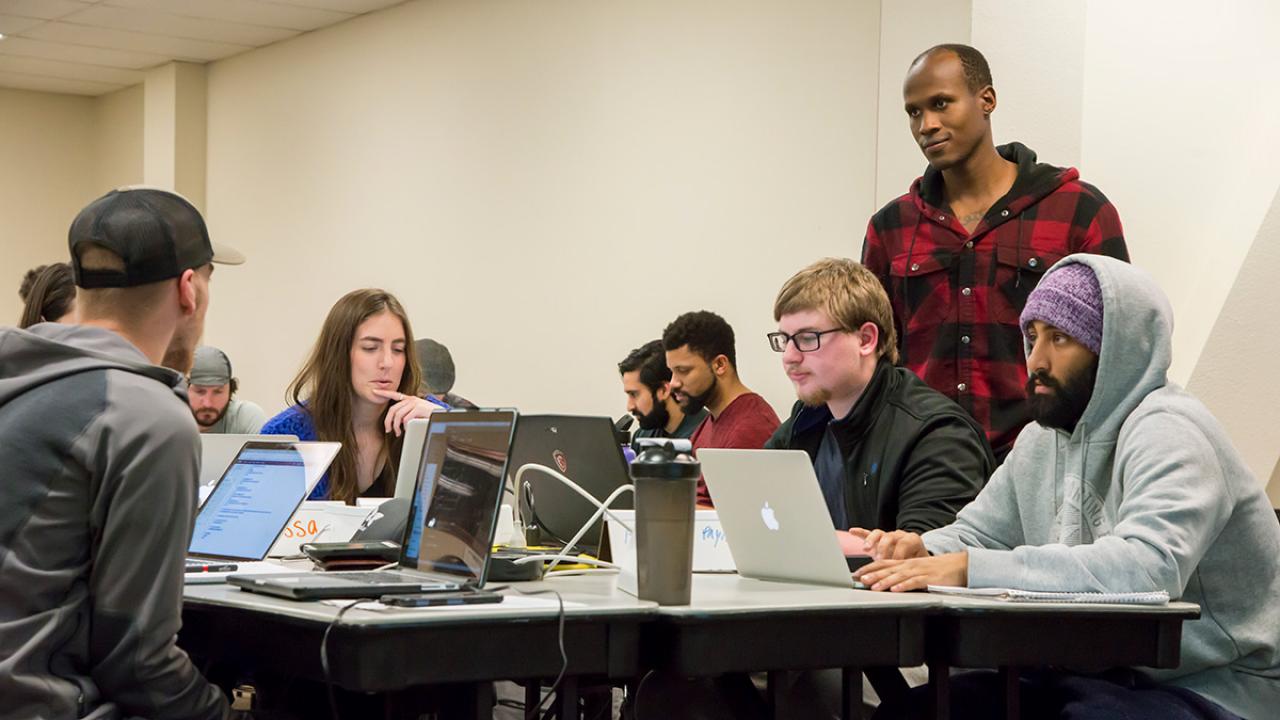 Instructor Nelly Sugira, standing to the right, helps students with a code-stringing exercise at UC Davis Extension's Coding Boo
