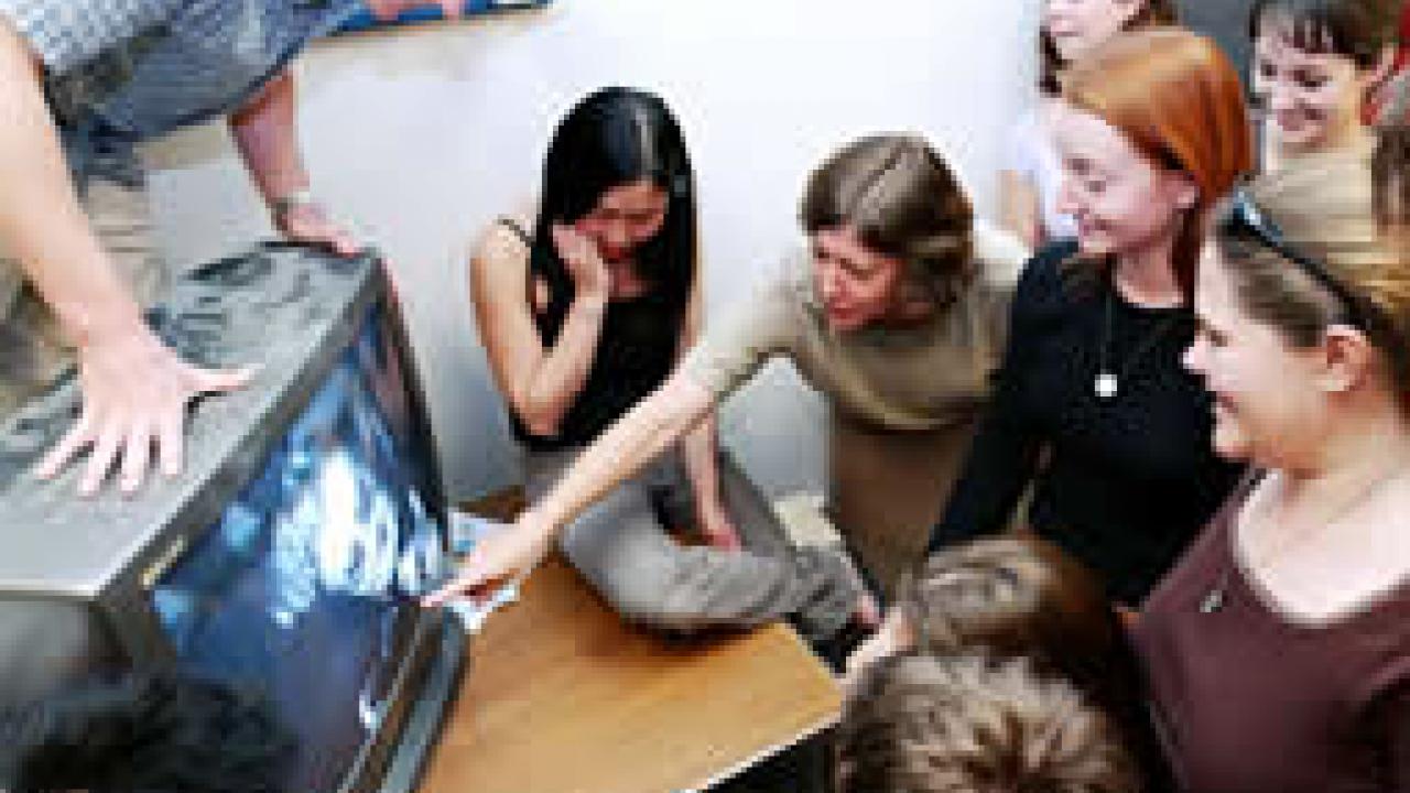 Photo: Woman  pointing to a television screen as younger woman watches
