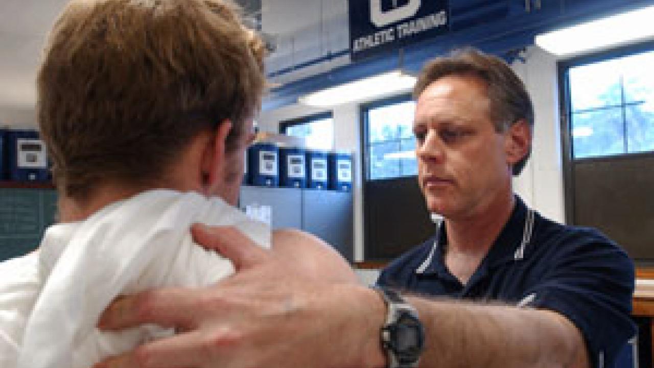 Jeff Hogan consults with an freshman football player about a possible strained muscle. It is one of Hogan&rsquo;s many duties as head trainer. He also helps keep the focus on the &ldquo;student athlete&rdquo; and to lead drug education efforts so the campus