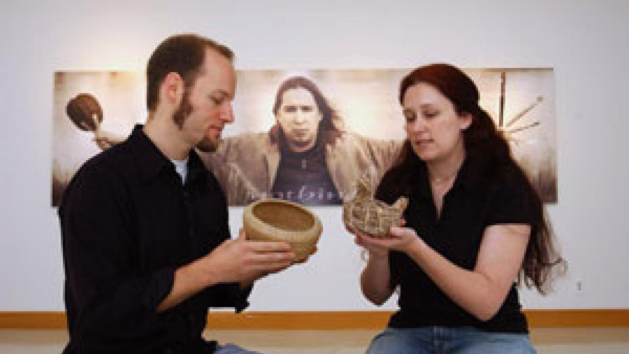 A photography exhibit by Shelley Niro provides the backdrop as 
Native American studies graduate students Michael Grofe and Lisa Woodard examine pine needle and sage baskets, respectively, in Carl Gorman Museum. The students say they are excite
