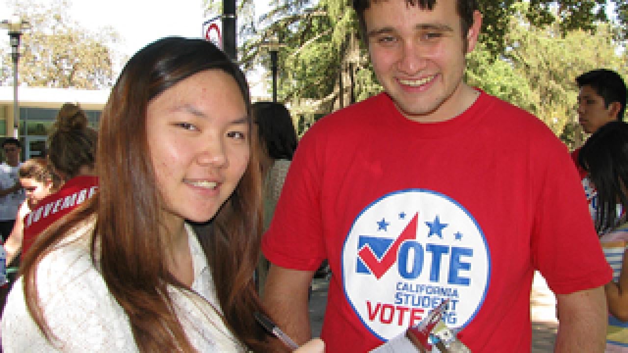 Woman with clip board with a man with a "vote" T-shirt