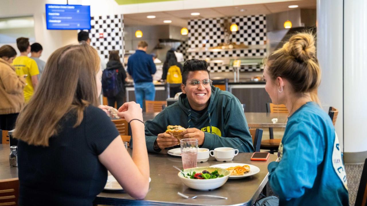 Three students, sitting around a table at a UC Davis dining commons, facing each other, eating and talking. 