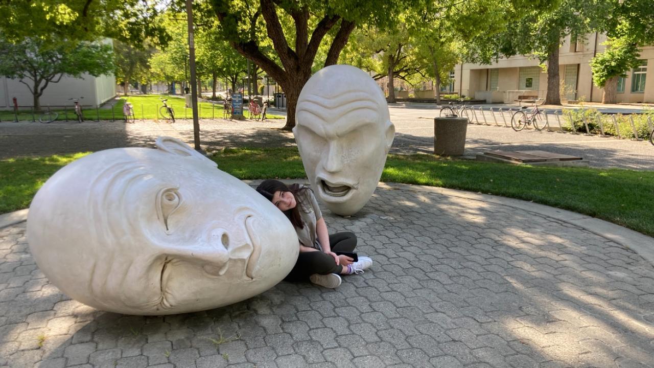 A picture of Jaimie Gelfond sitting in between the Yin & Yang Egghead sculpture.