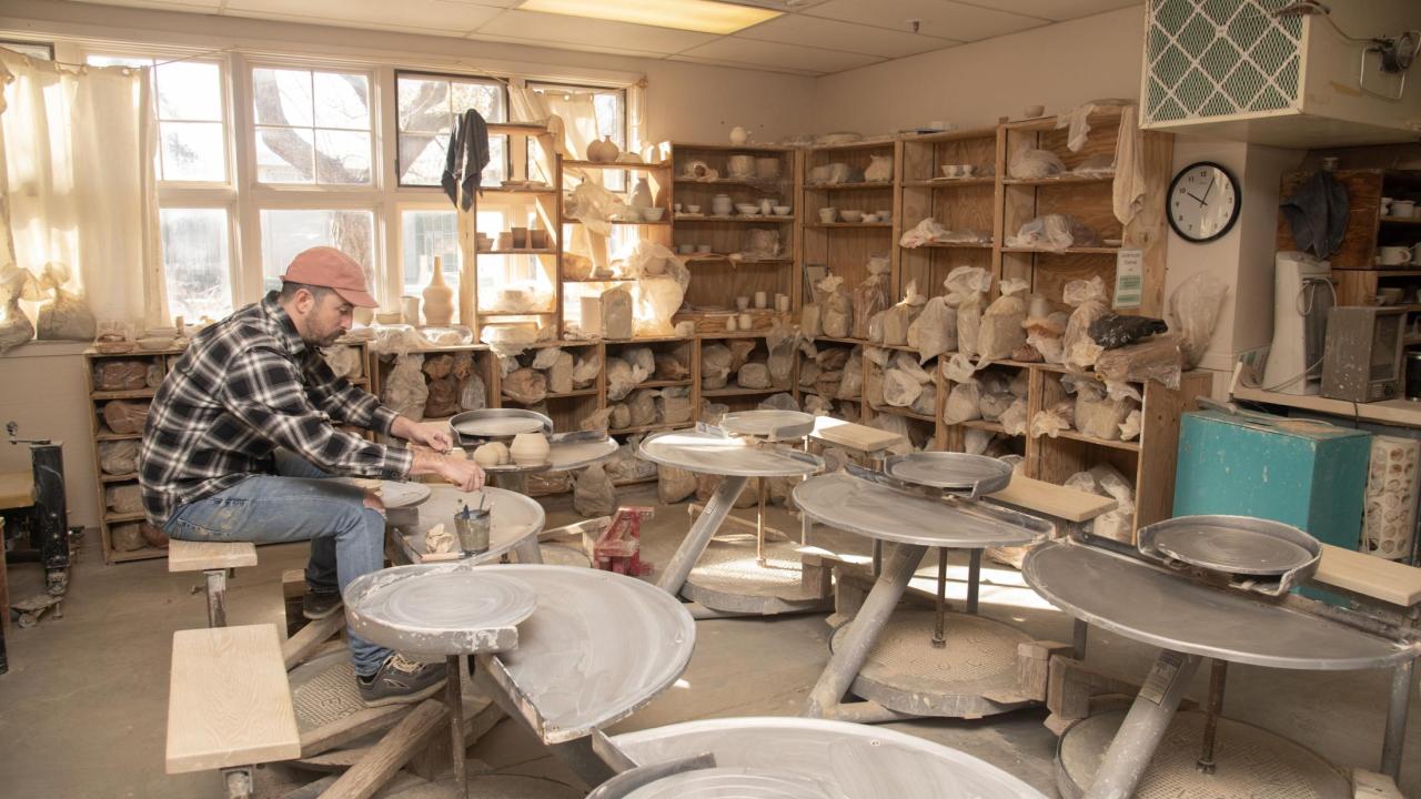 A person at a pottery wheel, shaping clay in a pottery studio.