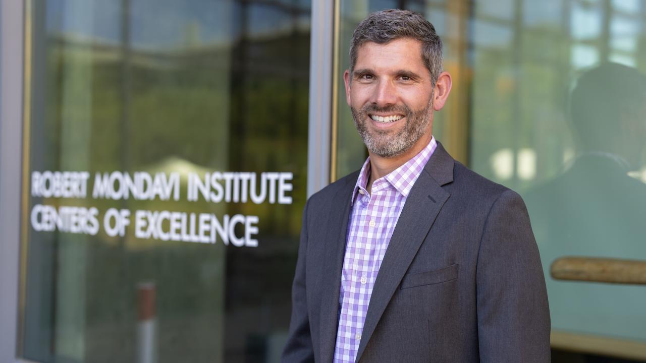 Ned Spang, associate professor of food science and technology, named new director of Robert Mondavi Institute. He stands in front of the institute's logo on a glass door. (Jael Mackendorf/UC Davis)