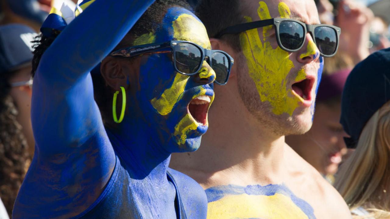 在一年一度的返校节足球赛上，一名男女学生身穿加州大学戴维斯分校（UC Davis）的蓝色和金色彩绘，为Aggies队加油助威
