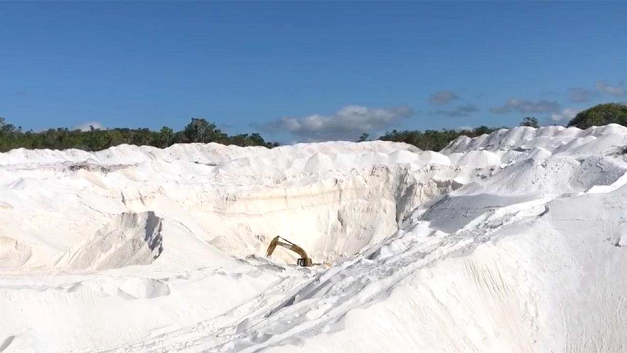 A quarry of bright white sand under a deep blue sky. An excavating machine can be seen in the distant center. 