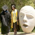 Photo: Two women in commencement gowns and mortar board hats near an Egghead sculpture