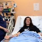 Photo: Apheresis nurse Natalie Detwiler stands beside hospital bed; Joanna Friesner is in the bed, with tubes in her arms for stem cell donation.