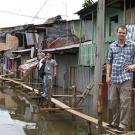 People standing on boards over a river with shacks behind them