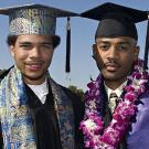 Photo: two graduates, one in colorful mortar board, the other with a purple lei