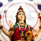 Hindu goddess statue of woman with dark hair holding red lotus bouquets in outstretched hands.