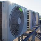 Oblique view of air conditioner units on a rooftop. A technician wearing a high visibility vest and hard hat is in the background. 