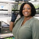 Woman stands in a lab and holds up a small crab in her right hand