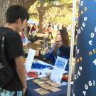 Students at table talk to other students with banner in foreground: Aggies helping Aggies