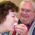 Man feeds strawberry dipped in whipped cream, to woman