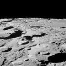 Monochrome view of a rocky, cratered plain with a black sky in the background.