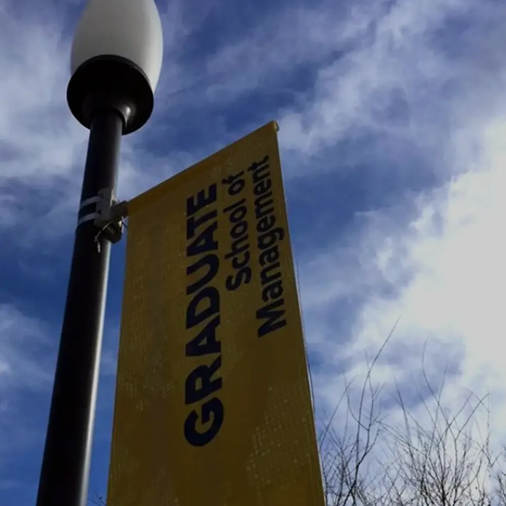 A light post with a banner for the Graduate School of Management at UC Davis in front of blue sky with clouds.