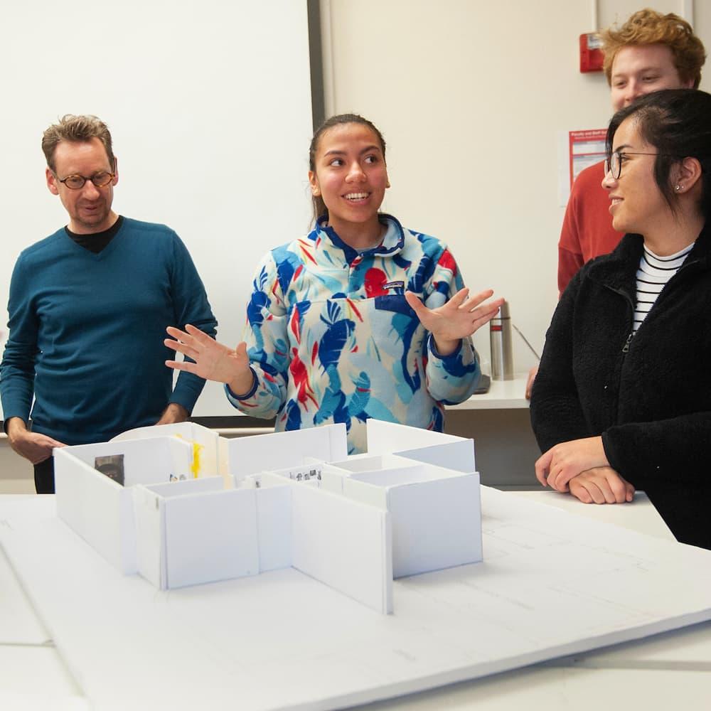 三名学生和一名教授在设计课上看一个建筑模型。